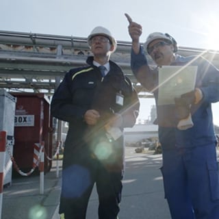 Dos operarios en un polígono industrial examinan sistemas de fluidos.